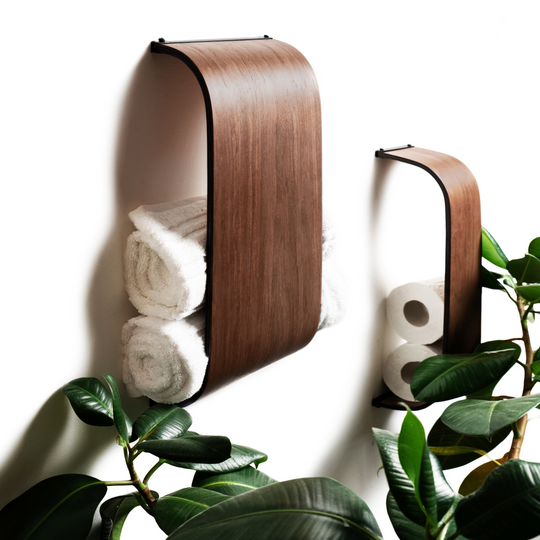 Wall-mounted wooden towel and toilet paper holders with a sleek curved design, elegantly storing rolled towels and paper rolls. Surrounded by greenery.