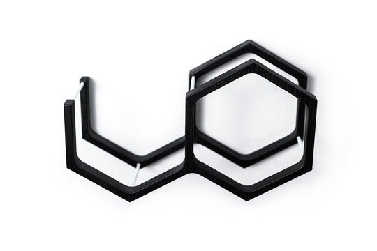 Close-up of a wall-mounted black mini honeycomb toilet paper holder. The holder features metal bars for support and a geometric design with textured wood.